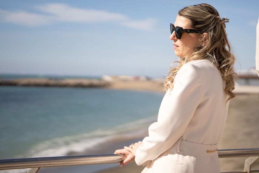 A couple stands along a seaside railing enjoying an ocean view in the bright sunny weather.