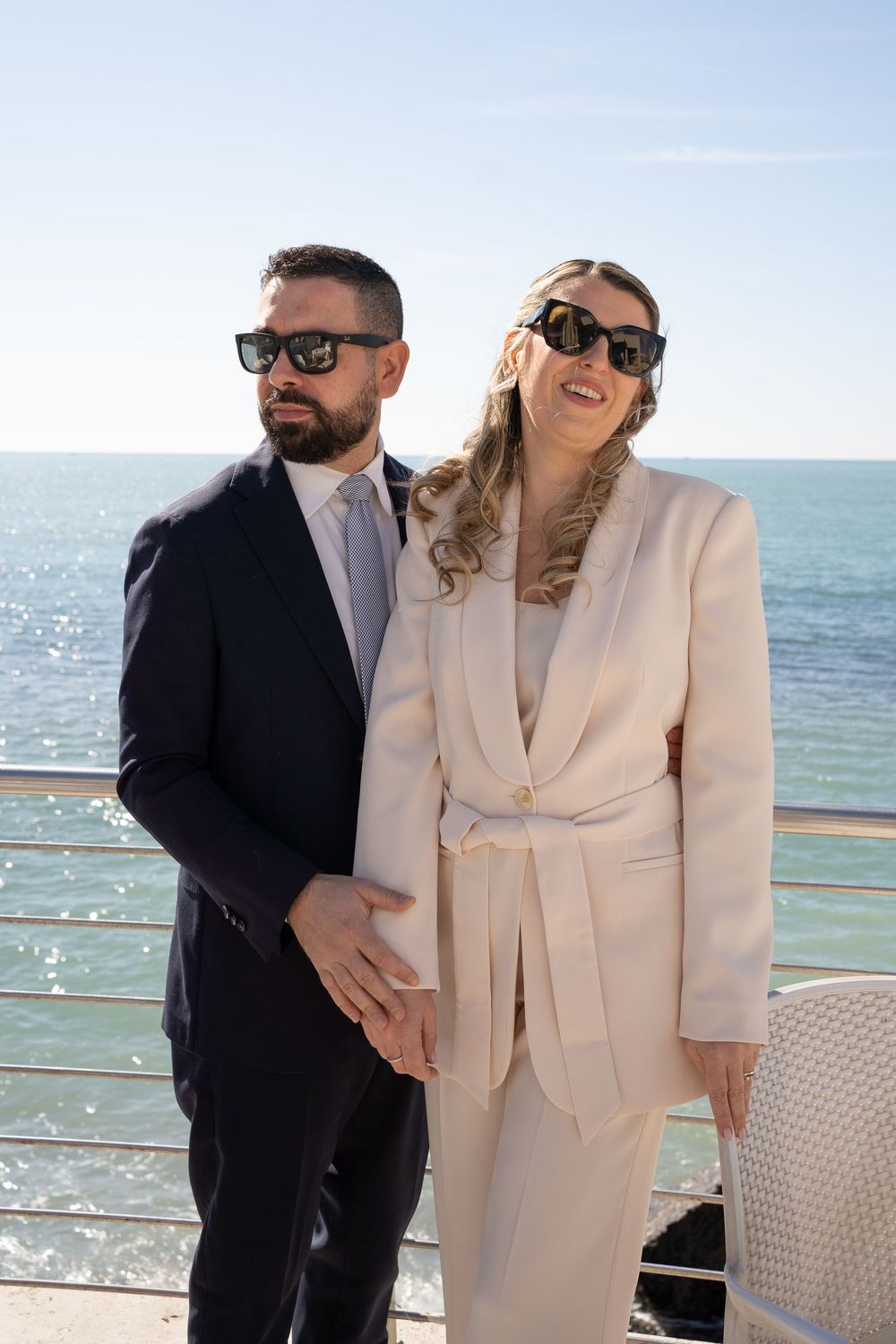 Happy couple in contrasting black and cream outfits share a romantic moment on an oceanfront balcony.