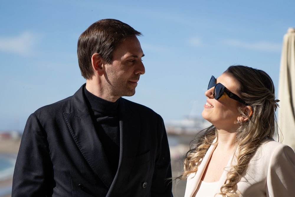 Couple shares a romantic moment by the ocean under bright blue skies.