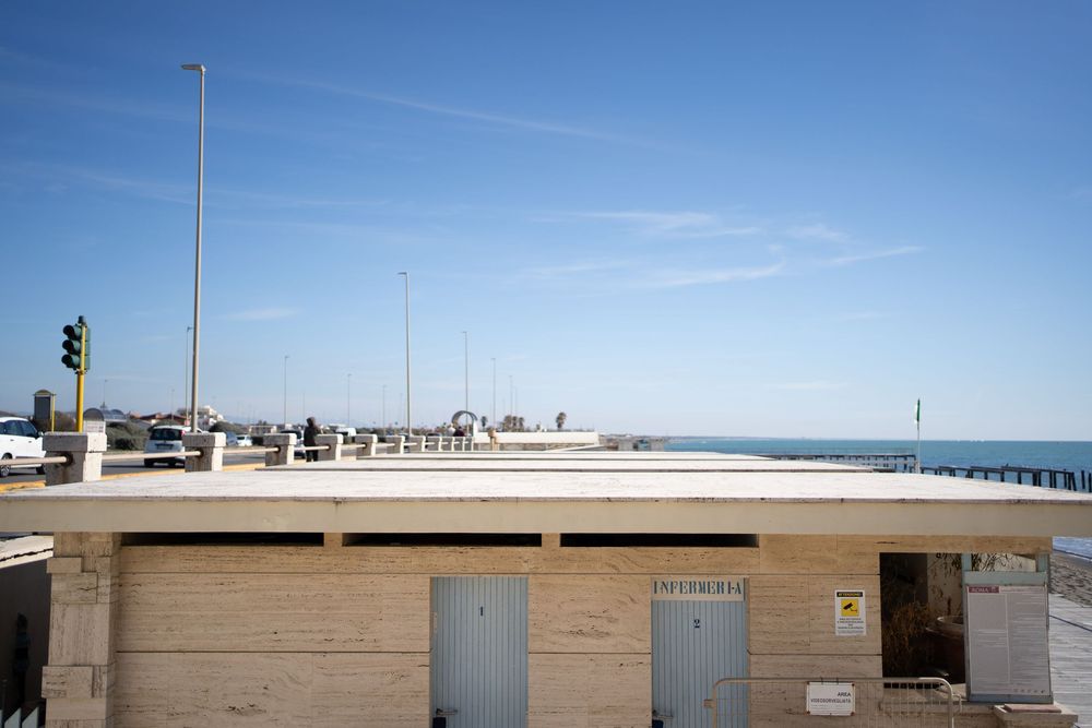 Empty beach boardwalk with light poles and buildings under bright blue sky.