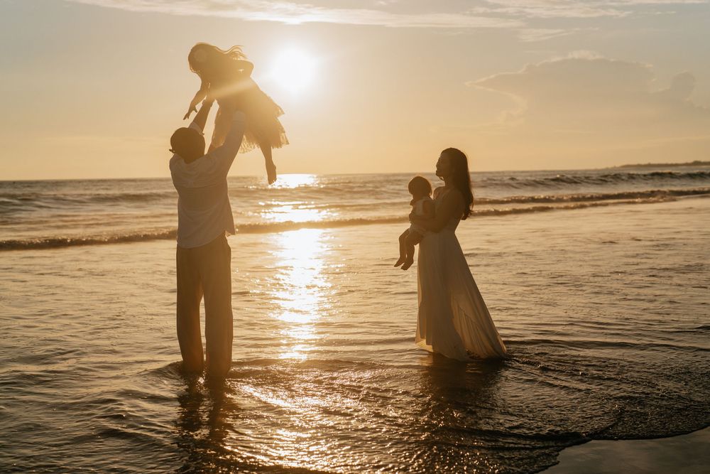 Silhouettes of people embracing on beach at sunset with golden light reflecting on water.