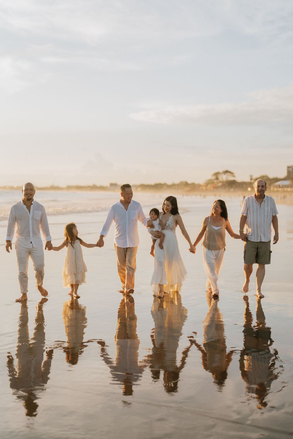 Row of people holding hands while standing in shallow beach water with perfect reflections.