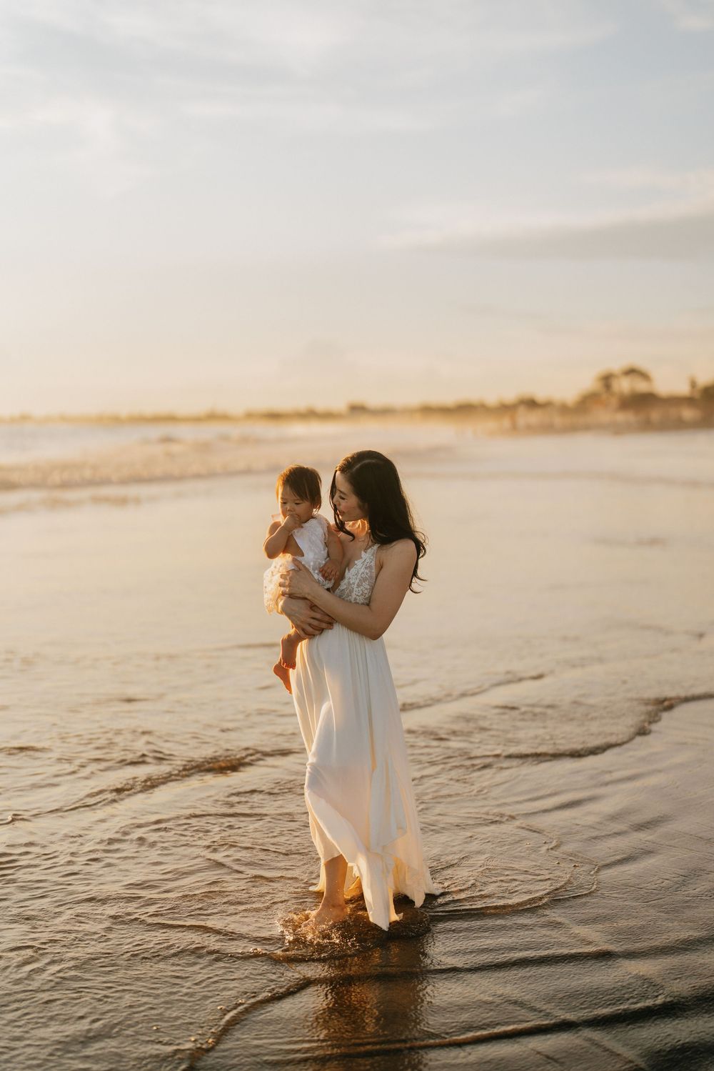 People playing in shallow ocean water during golden hour with gentle waves.