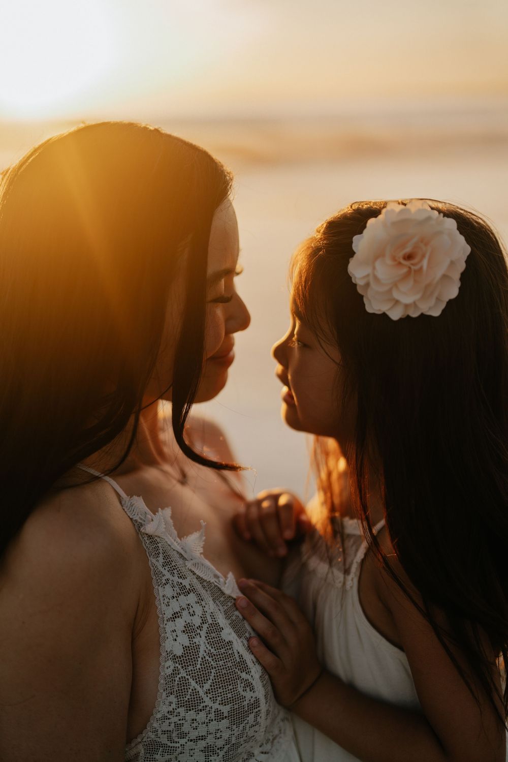 Close-up silhouettes in warm sunset light with white flower hair accessory.