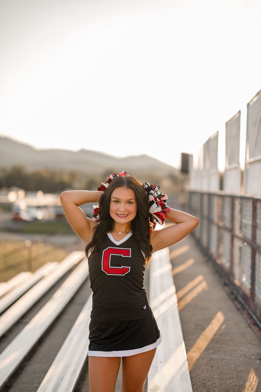 A cheerleader in black uniform poses on stadium bleachers during a golden sunset photoshoot.
