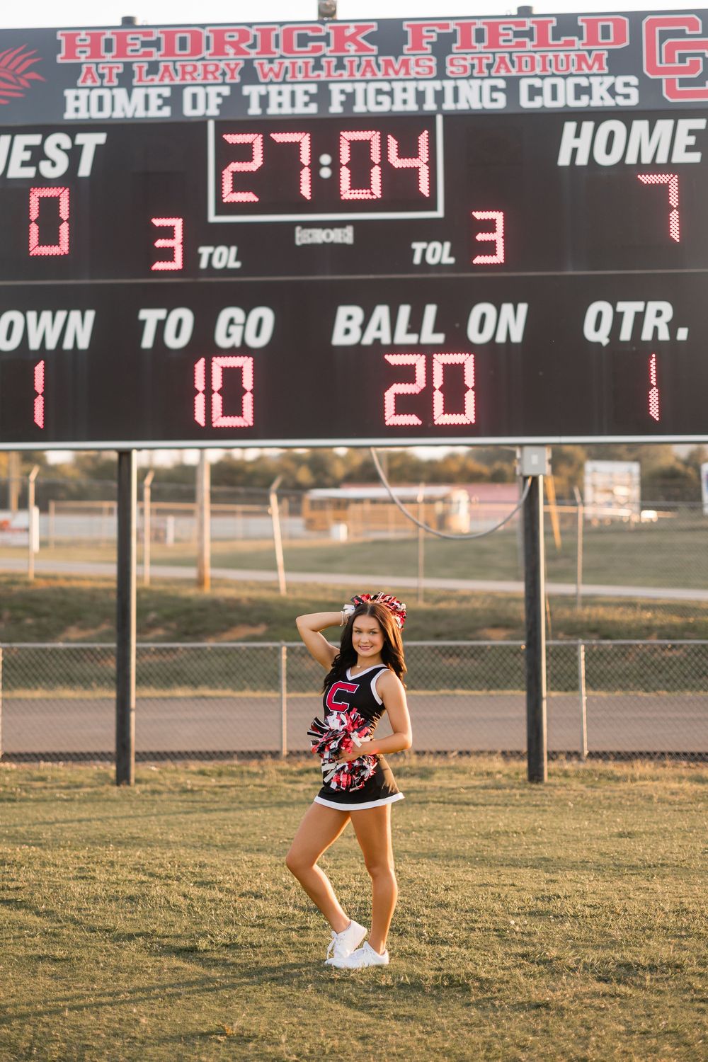Cheerleader performs split leap in front of football stadium scoreboard during golden hour.