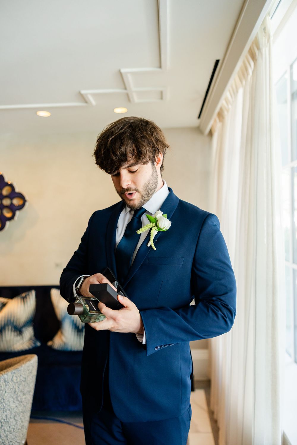 Groomsman in navy blue suit checks his phone while wearing a white boutonniere in an elegant indoor setting.