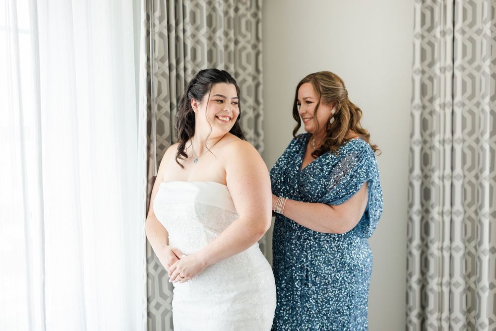 Two people in a white dress and blue dress sharing an intimate moment in front of a patterned curtain.
