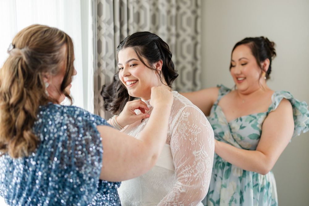 Group of bridesmaids in blue floral dresses help the bride get ready in a bright sunlit room.