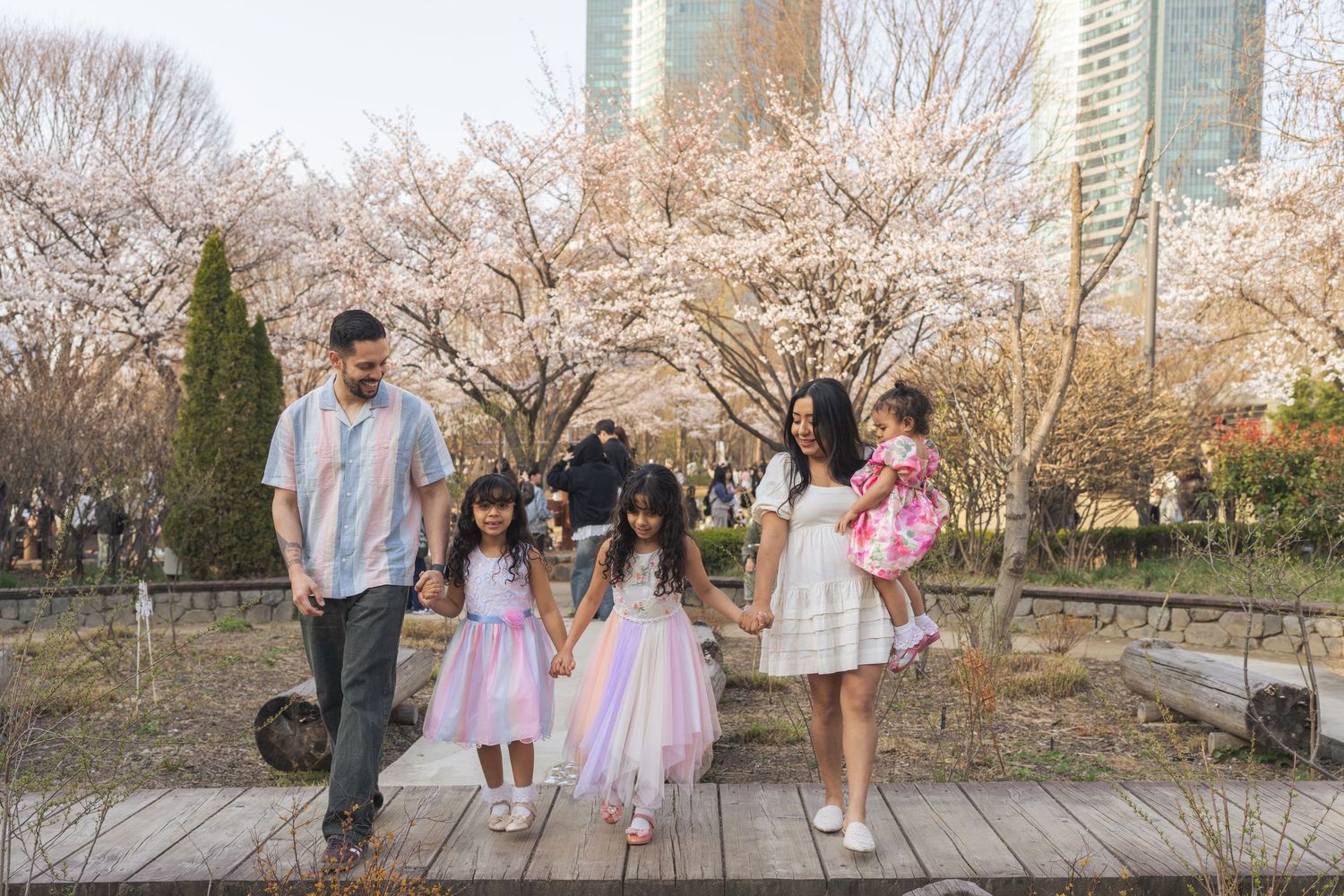 A group walks together under blooming cherry blossom trees in a spring garden setting.