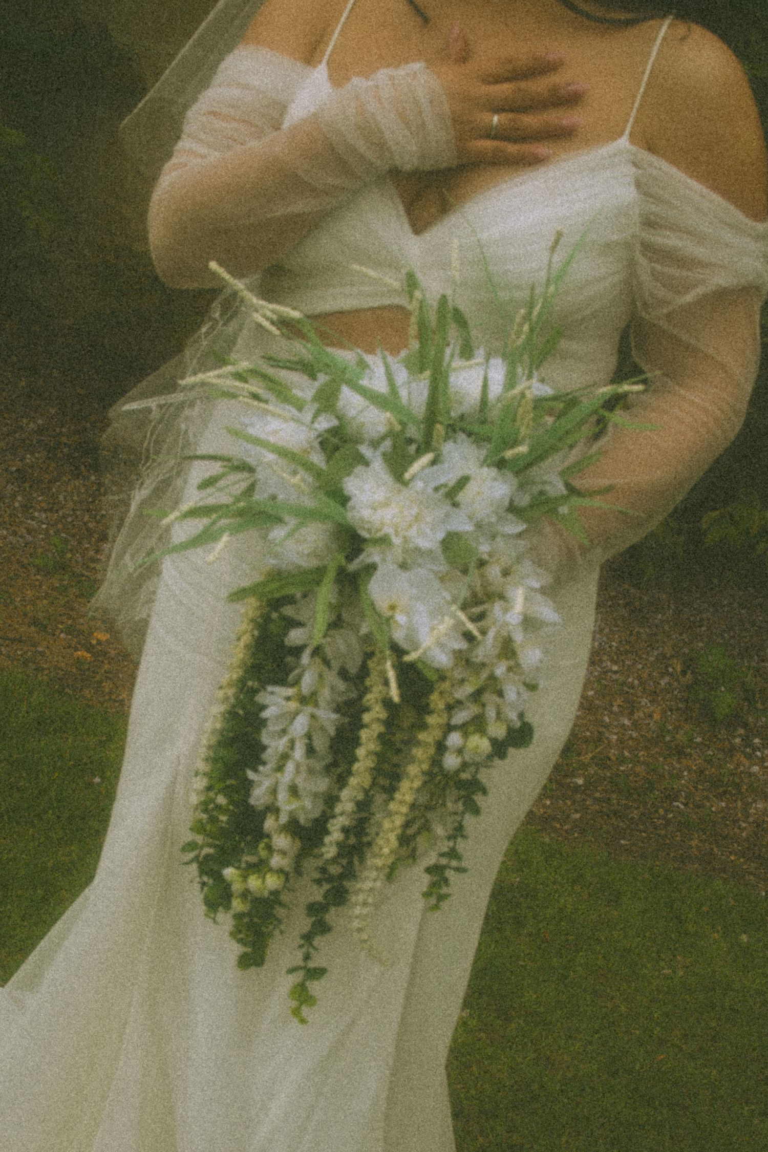 A vintage-style wedding photo showing a cascading white floral bouquet against an elegant ivory wedding dress.