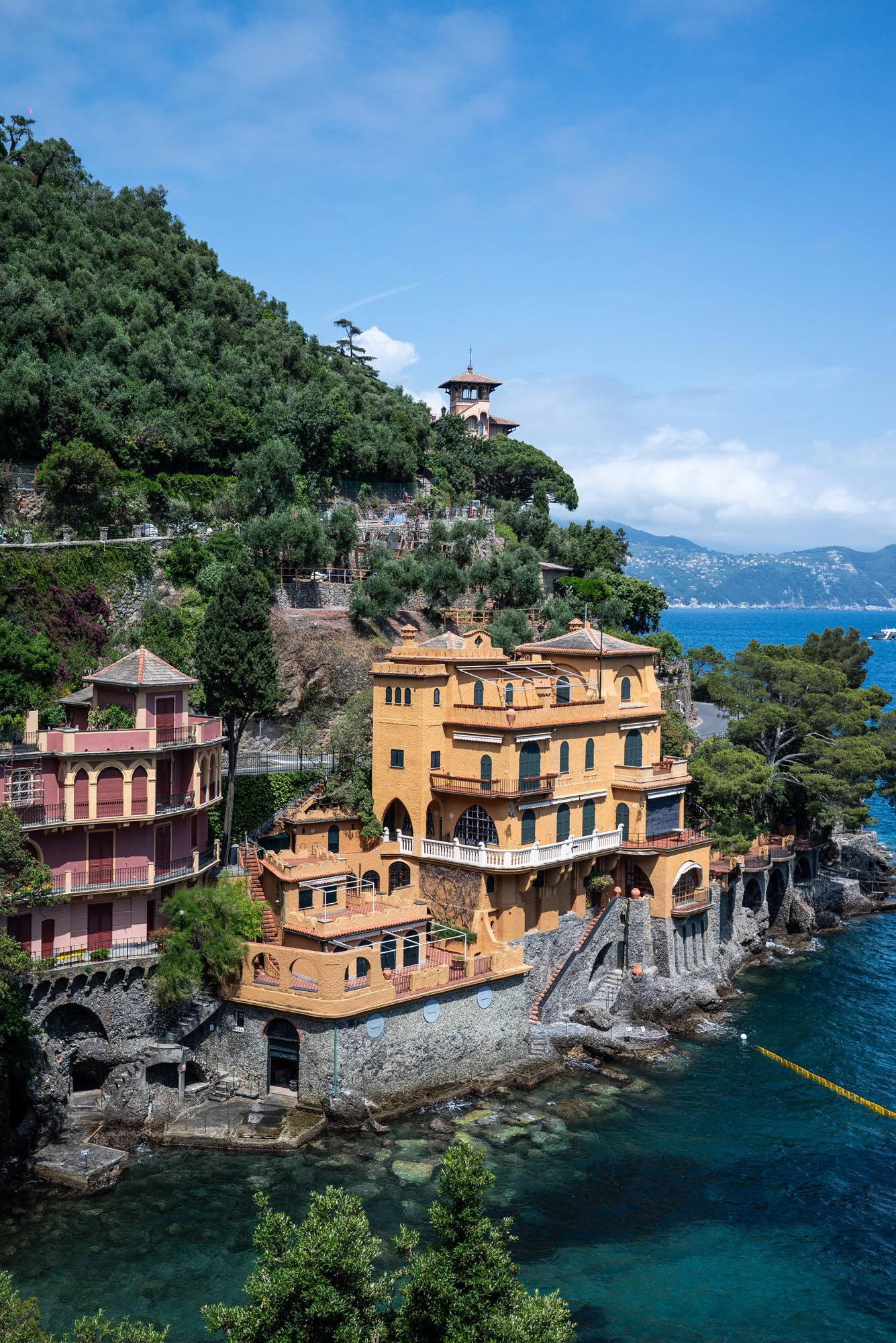 A luxurious yellow villa perched on rocky cliffs overlooking the Mediterranean Sea in Portofino, Italy.