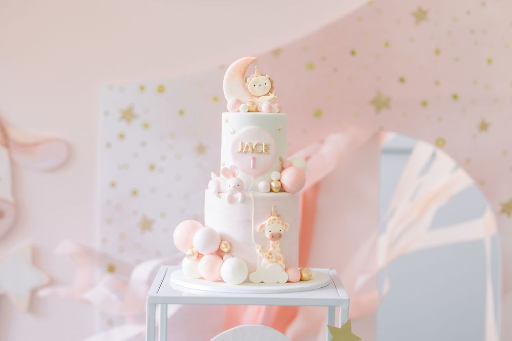 Elegant pastel pink and white three-tier birthday cake decorated with stars, moons and delicate macarons on a silver stand.