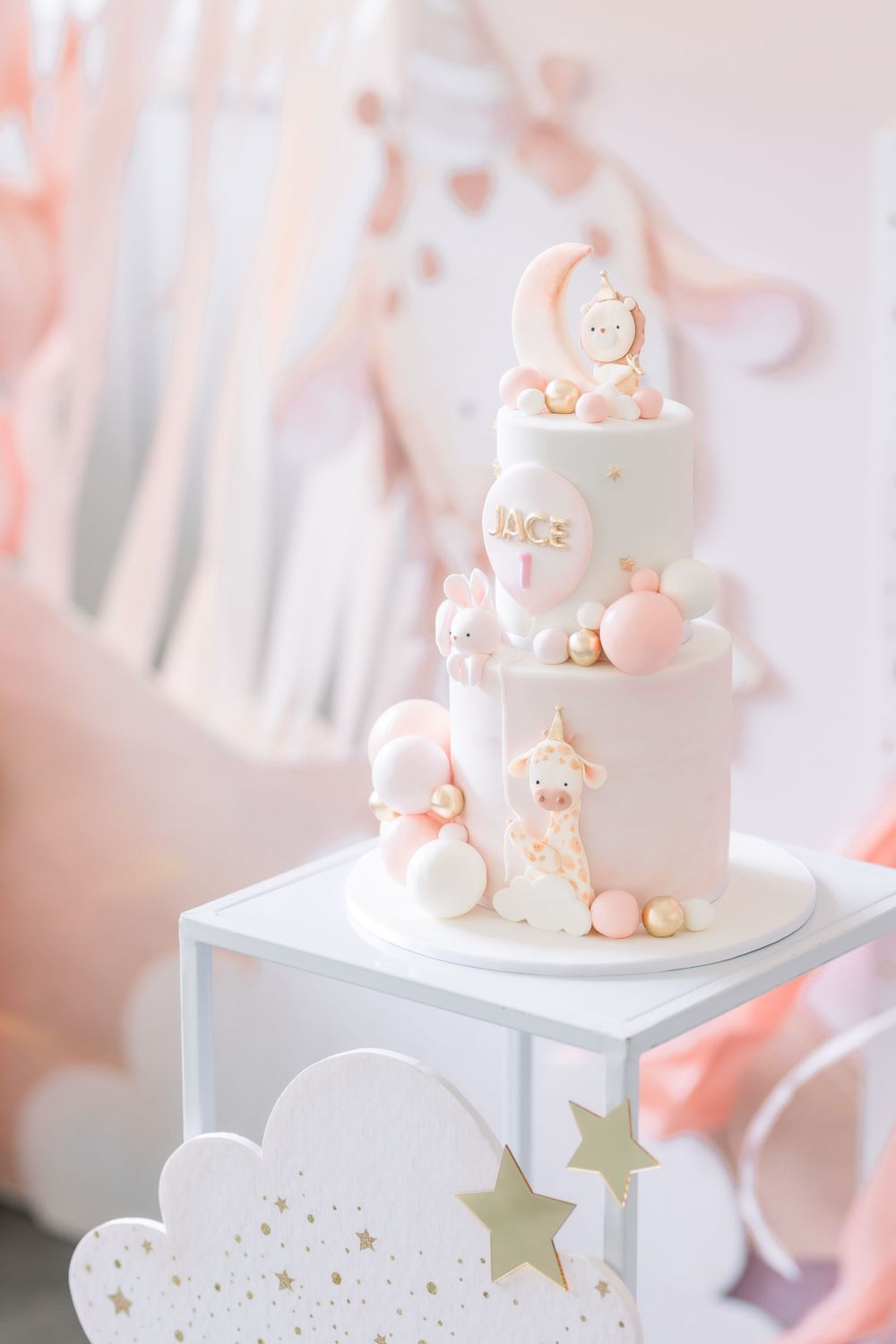 Elegant white tiered baby shower cake with delicate pink accents and cloud decorations on a white display stand.