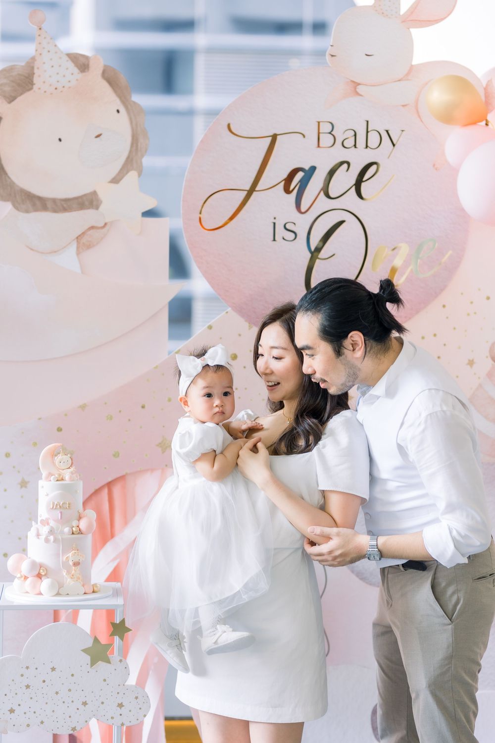 Pink and white themed celebration setup with decorative cake and cloud motif backdrop.
