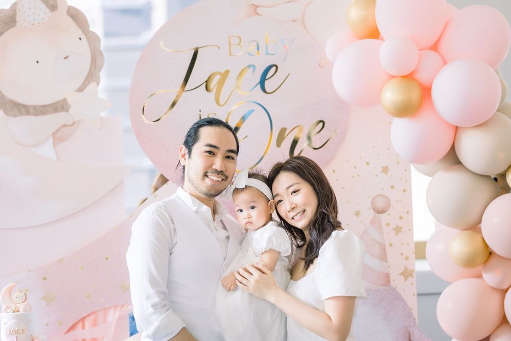 Pink and white balloon arch and party decorations create an elegant backdrop for a baby-themed celebration.