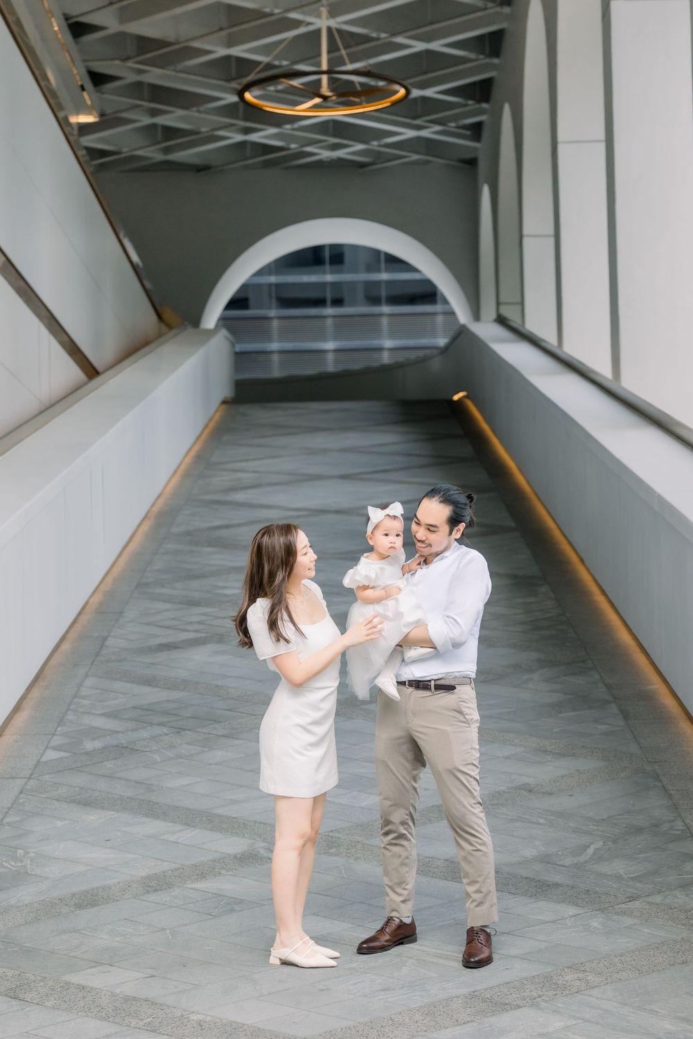 A family interacts playfully in a modern minimalist hallway with white walls and geometric architectural details.