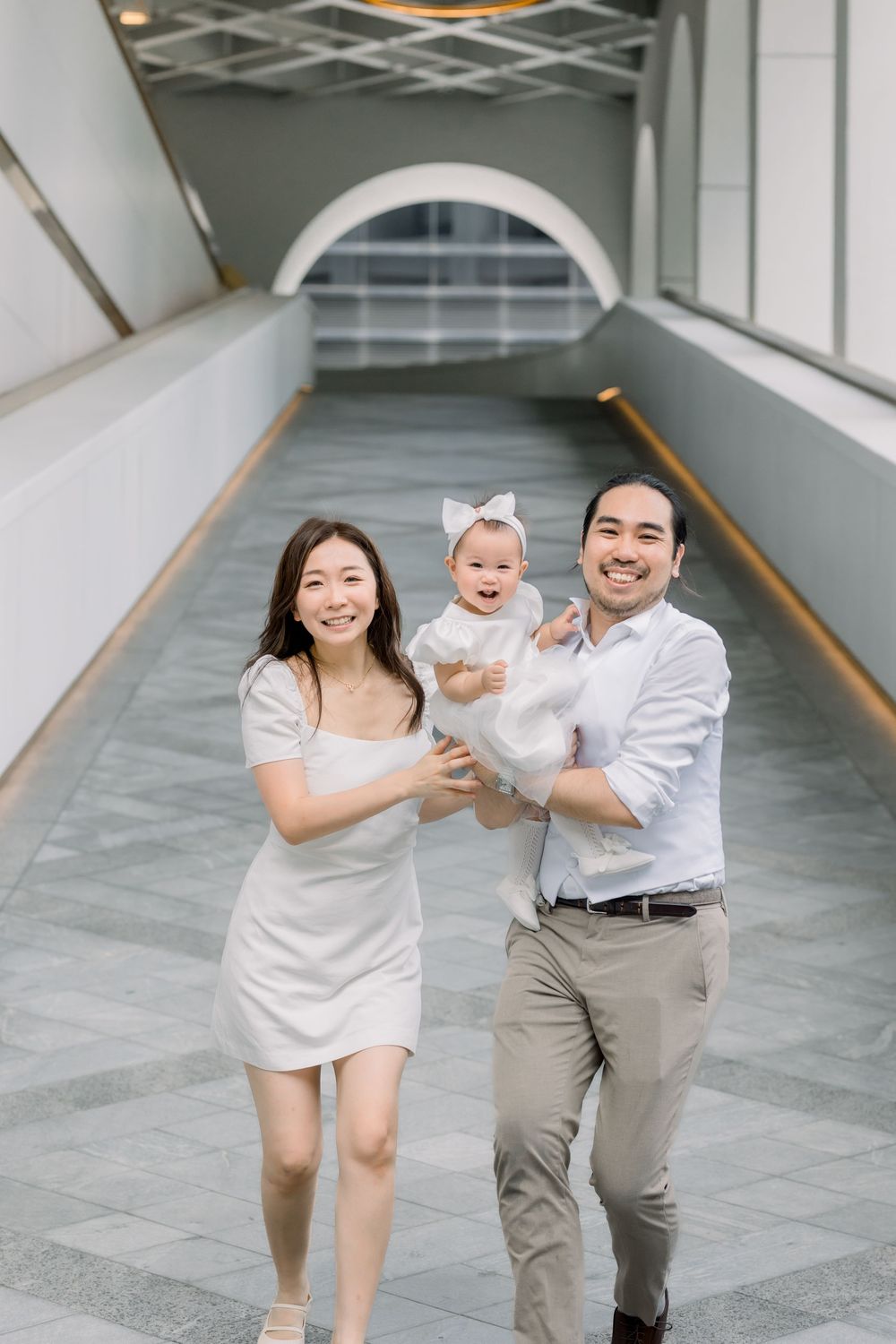 A happy family plays and walks together in a modern indoor hallway setting with white walls.