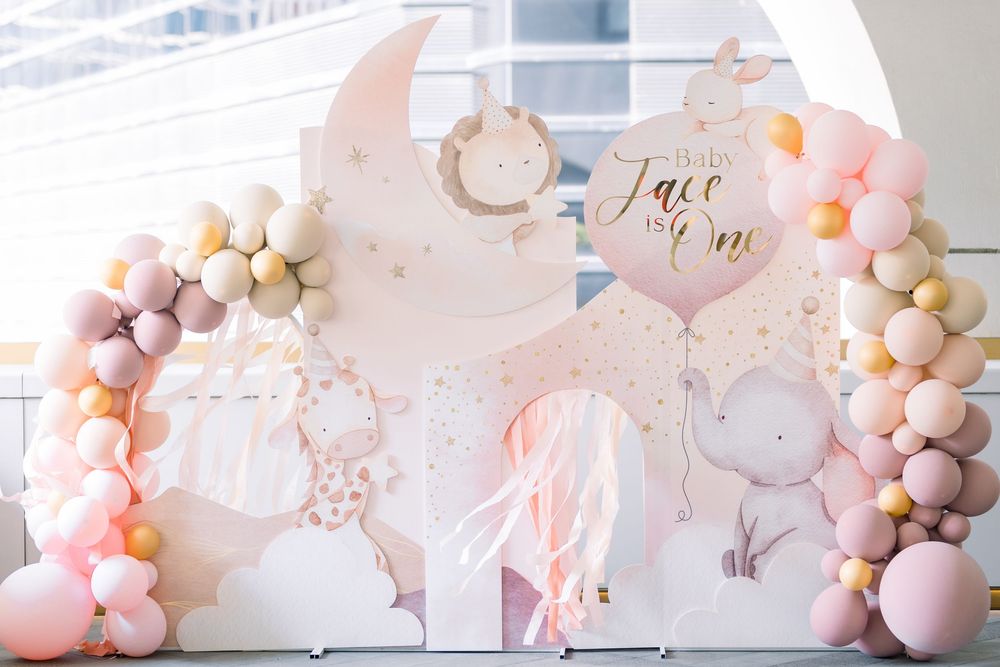 Pastel pink and gold balloon arch with floral accents creates an elegant party backdrop for a special celebration.