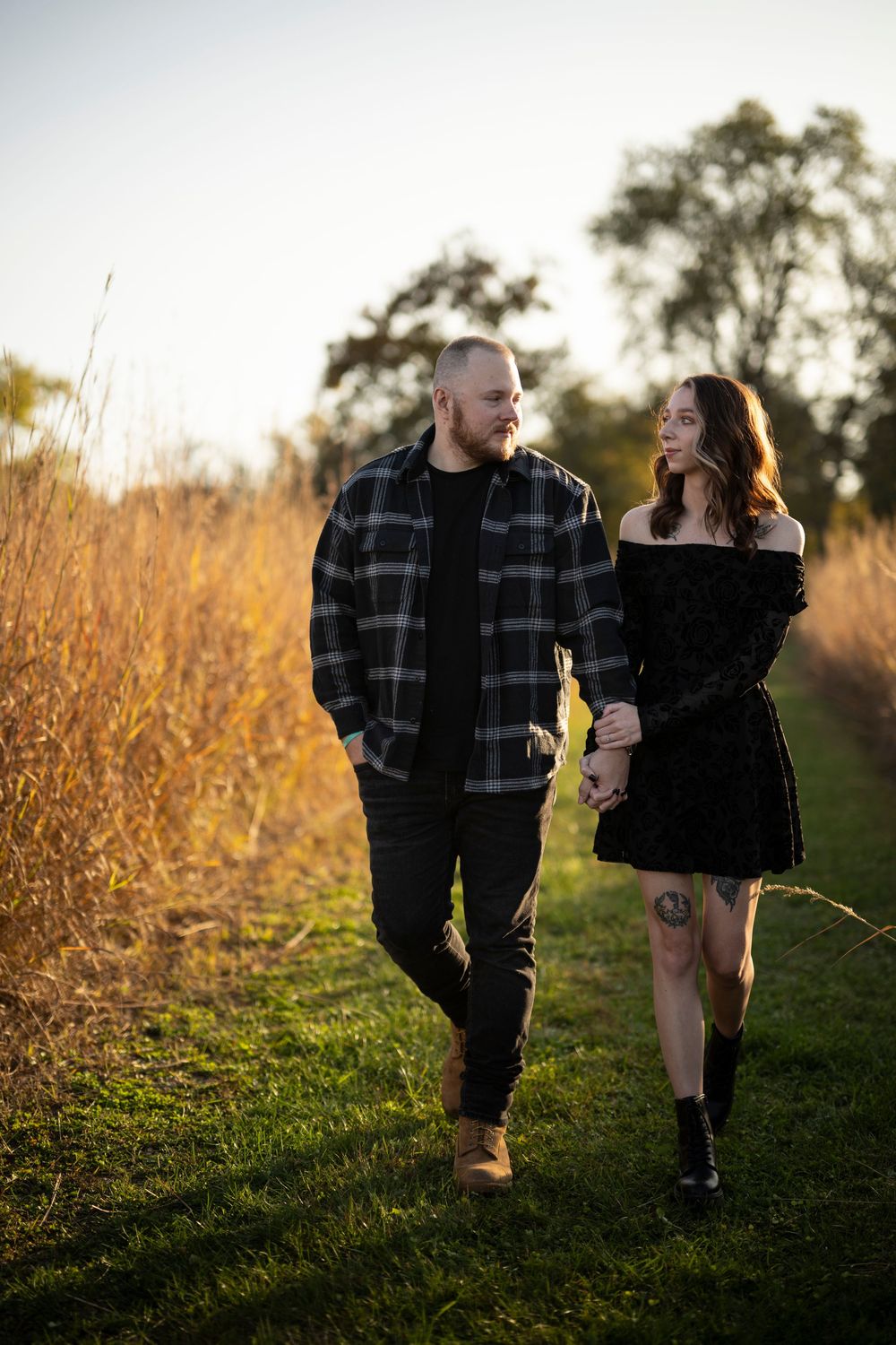 Couple walks together through tall golden grass at sunset.