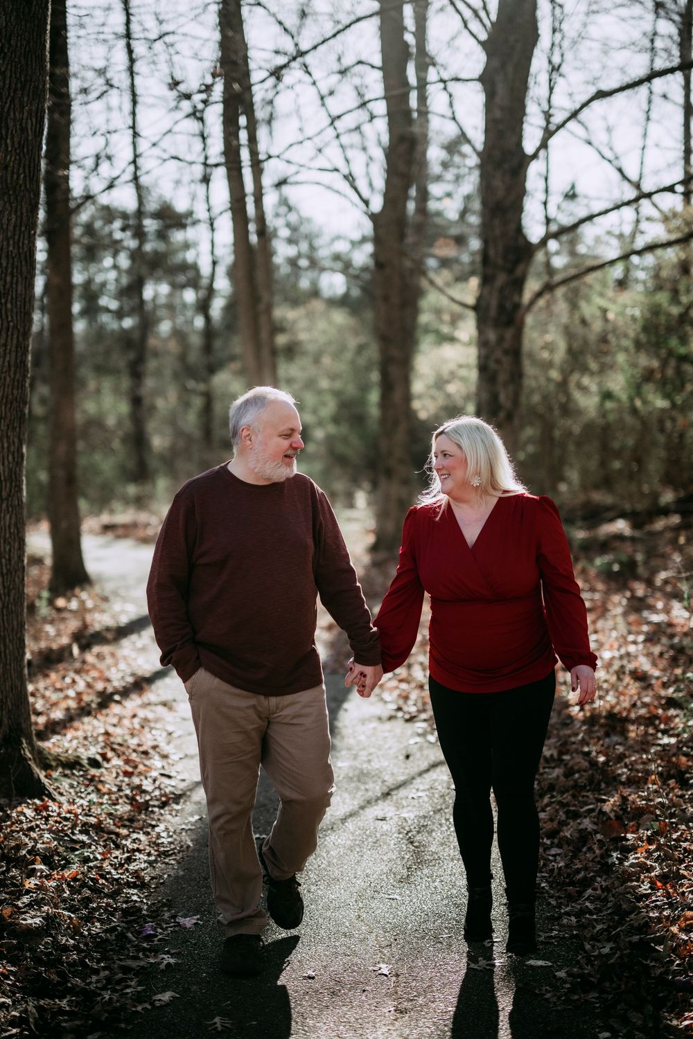 A couple enjoys a romantic walk holding hands on a wooded path in autumn.
