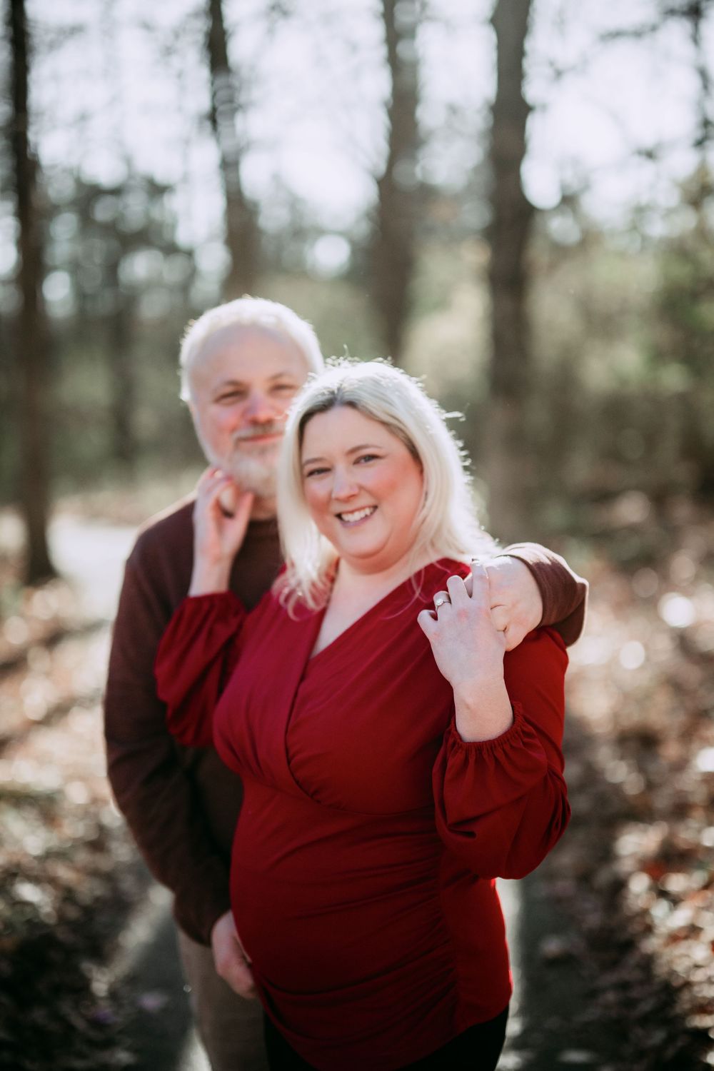 Couple in matching red sweaters laughs together in a forest setting.