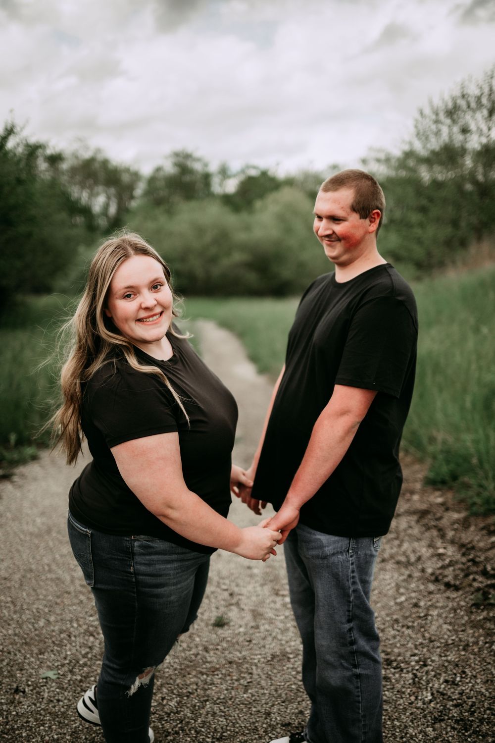 Casual couple sharing a playful moment while walking on a graveled path in nature.