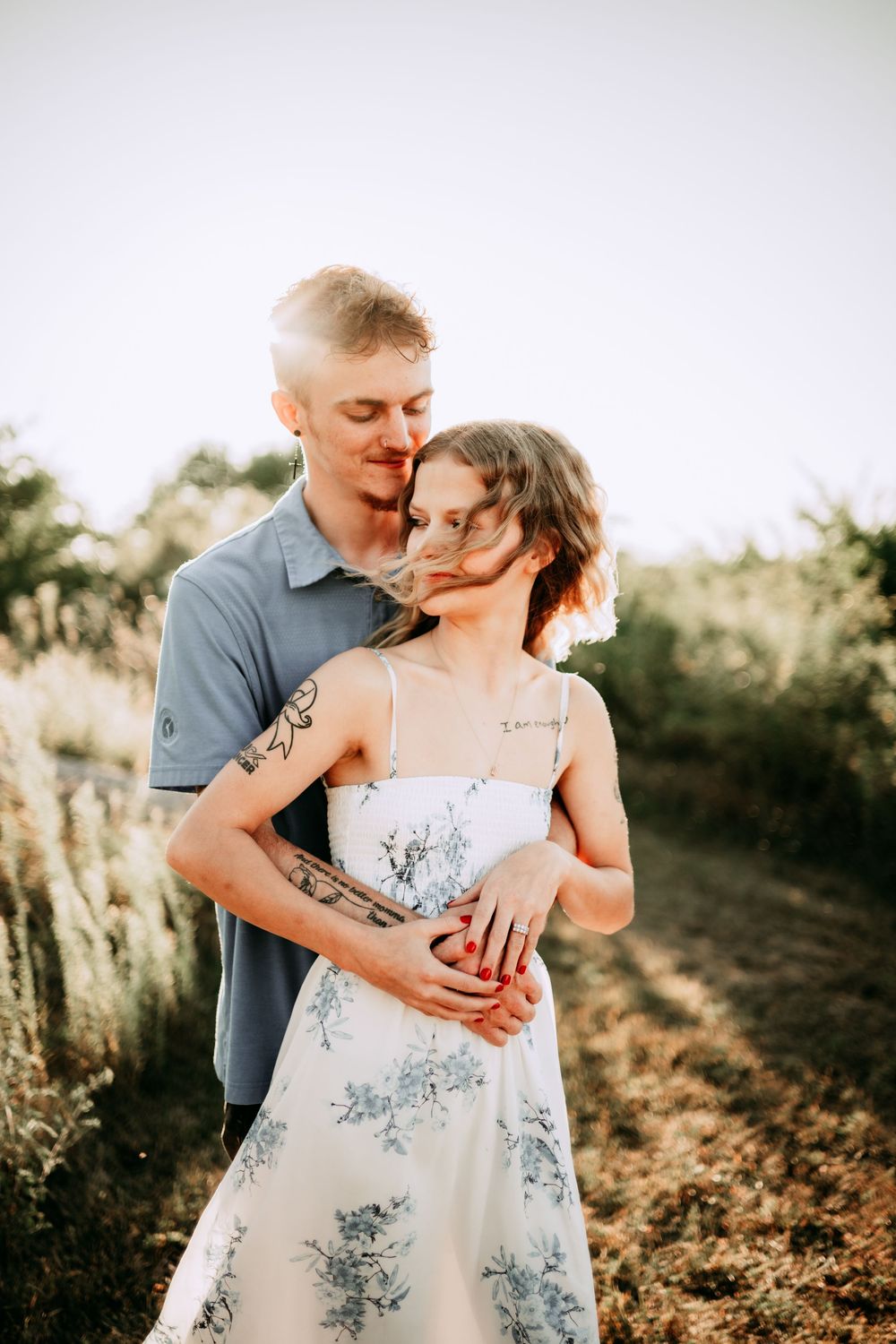 Romantic couple embraces in a sunlit field wearing casual summer attire.