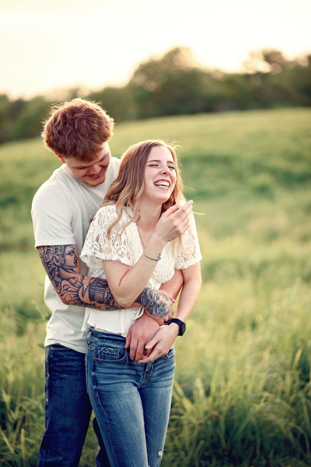 Couple laughing together in a sunny meadow wearing casual denim and white tops.