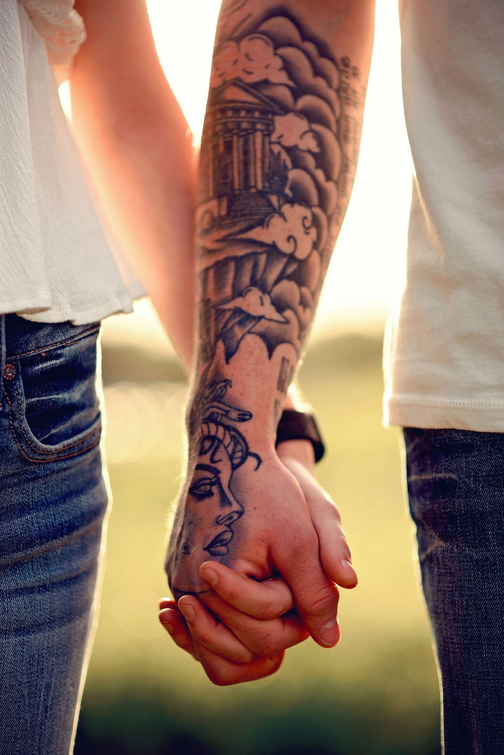 Close-up of tattooed hands holding each other against a sunset backdrop.