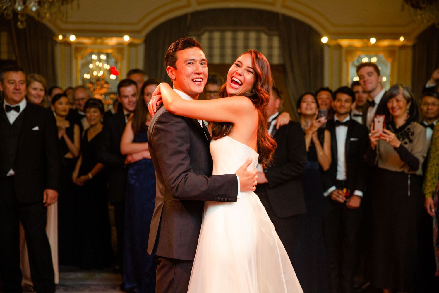 Couple sharing a dance moment surrounded by guests at an elegant venue.