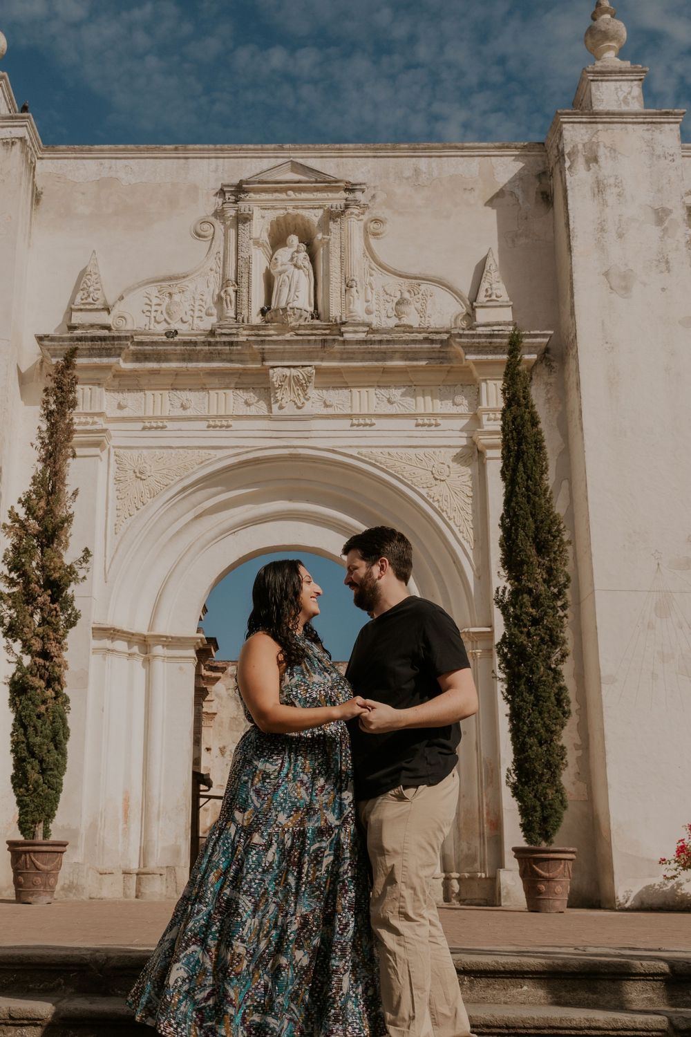 Couple shares intimate moment against white stone architecture with classical columns and archways during sunset.
