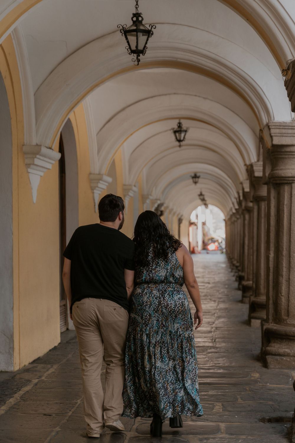 People walking through an elegant arched corridor with classical architecture and lantern lighting.