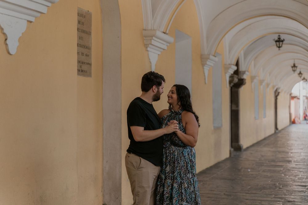 Romantic couple dancing and embracing in an elegant colonnade hallway with arched white columns.