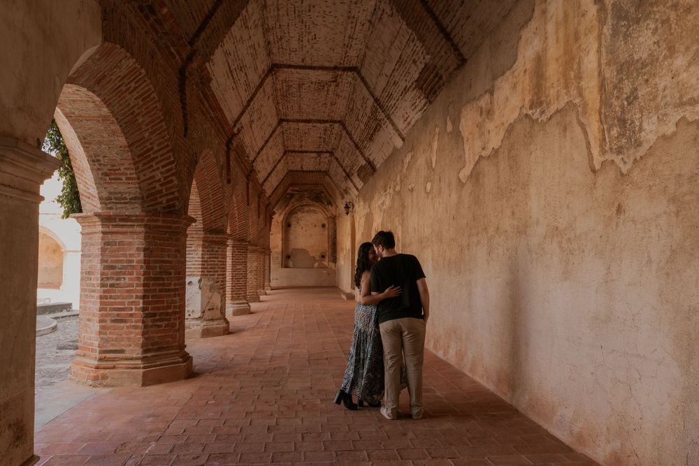 Ancient stone archway corridor with rustic columns leads into a shadowy walkway in an old building.