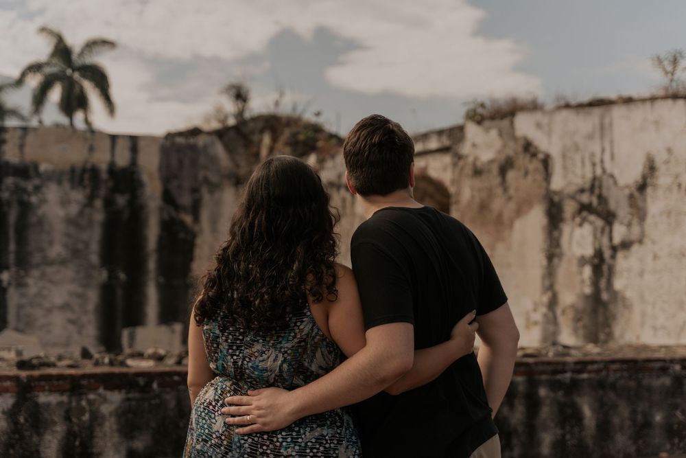 Two people walking close together through ancient stone ruins under moody, overcast skies.