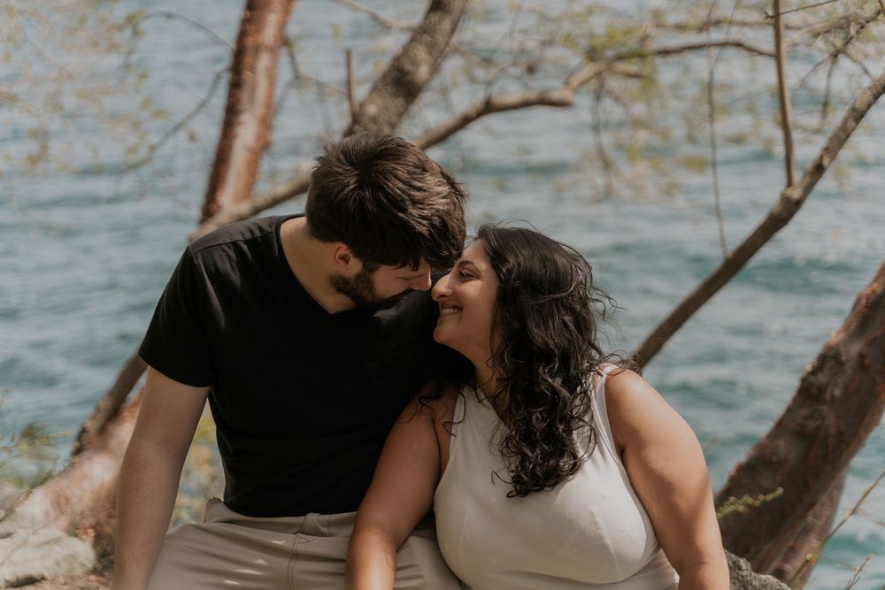 Couple shares an intimate moment near a lake with trees framing the scenic setting.