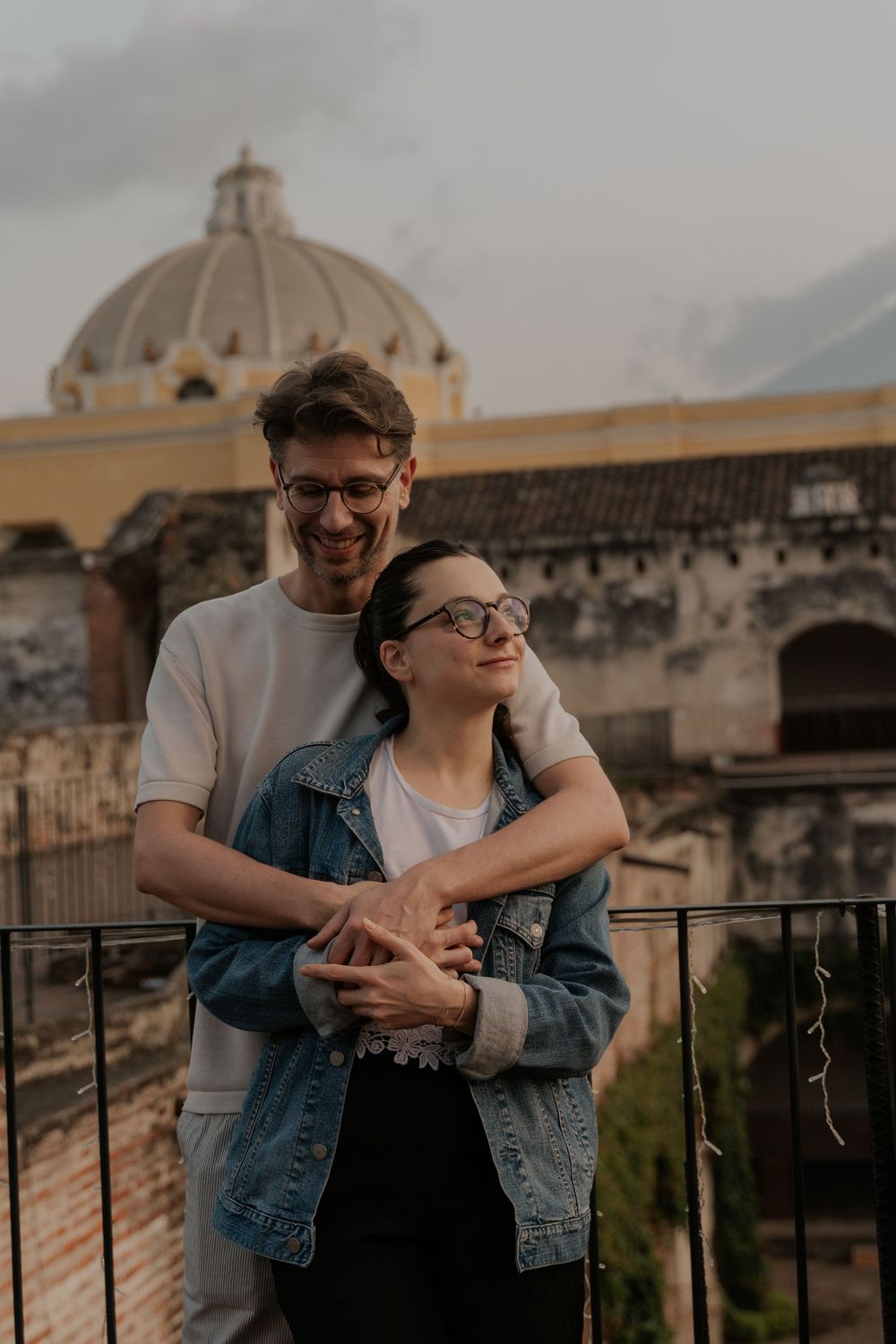 A couple shares romantic moments on a rooftop terrace overlooking historic domed architecture at sunset.