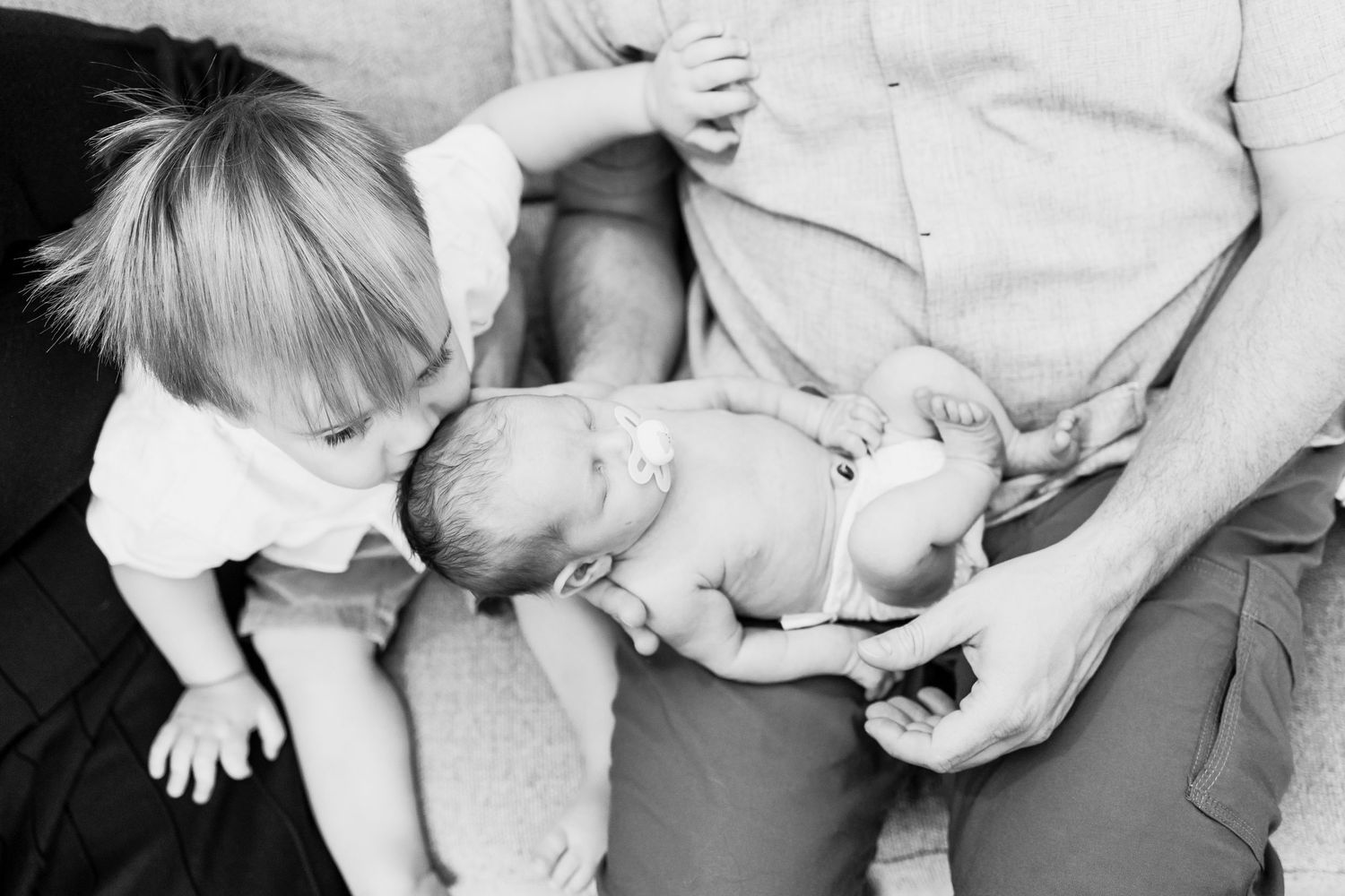 Black and white series of a sleeping newborn in soft white wrapping with sibling.