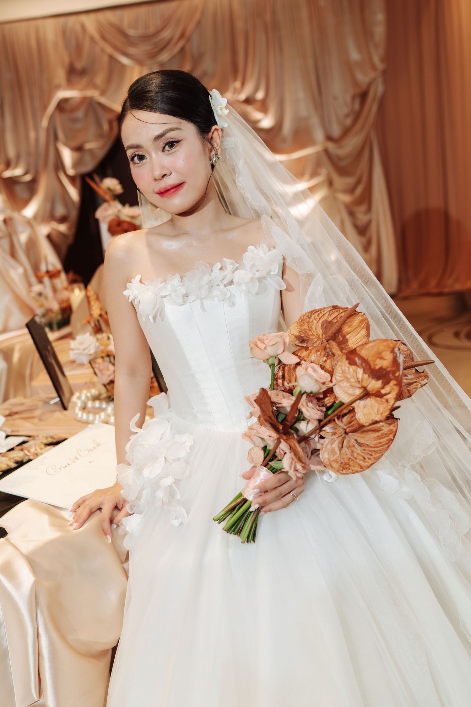 Asian bride in white strapless ballgown holding terracotta floral bouquet at wedding reception.