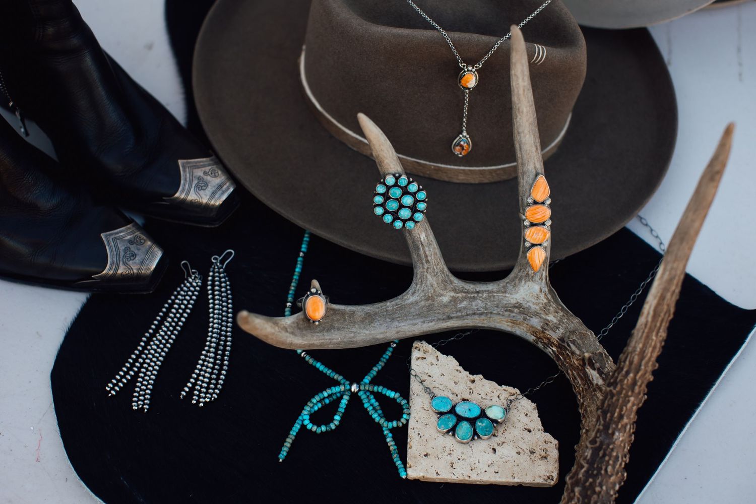 Western style accessories including a brown hat, antler decor, and turquoise jewelry arranged on a dark surface.