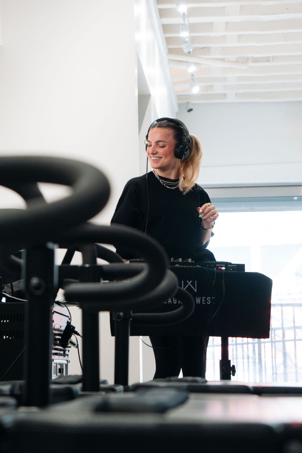 Someone in black attire working at a DJ setup in a bright indoor space.