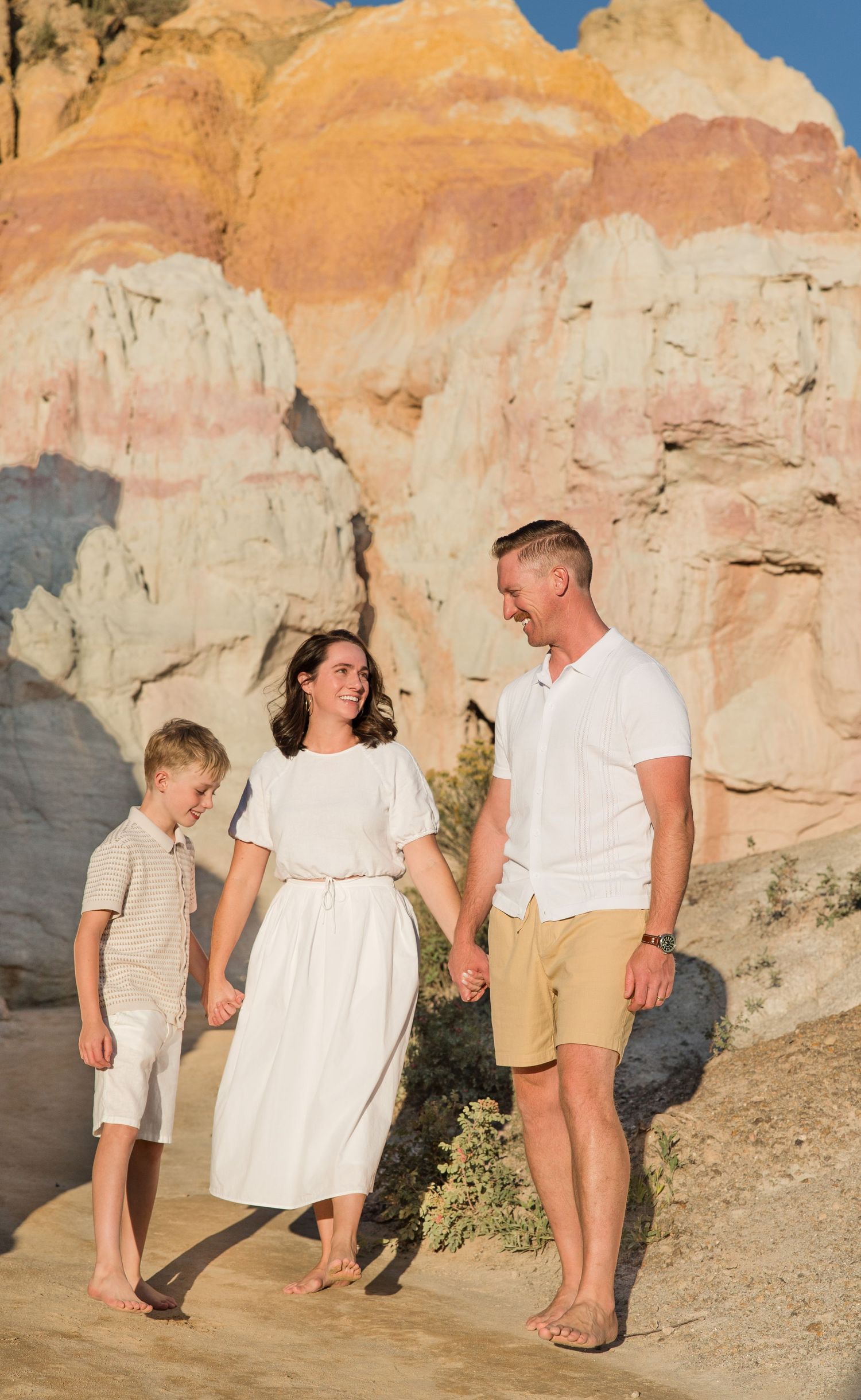 A family poses together in a field of tall grass with mountains in the background at sunset.