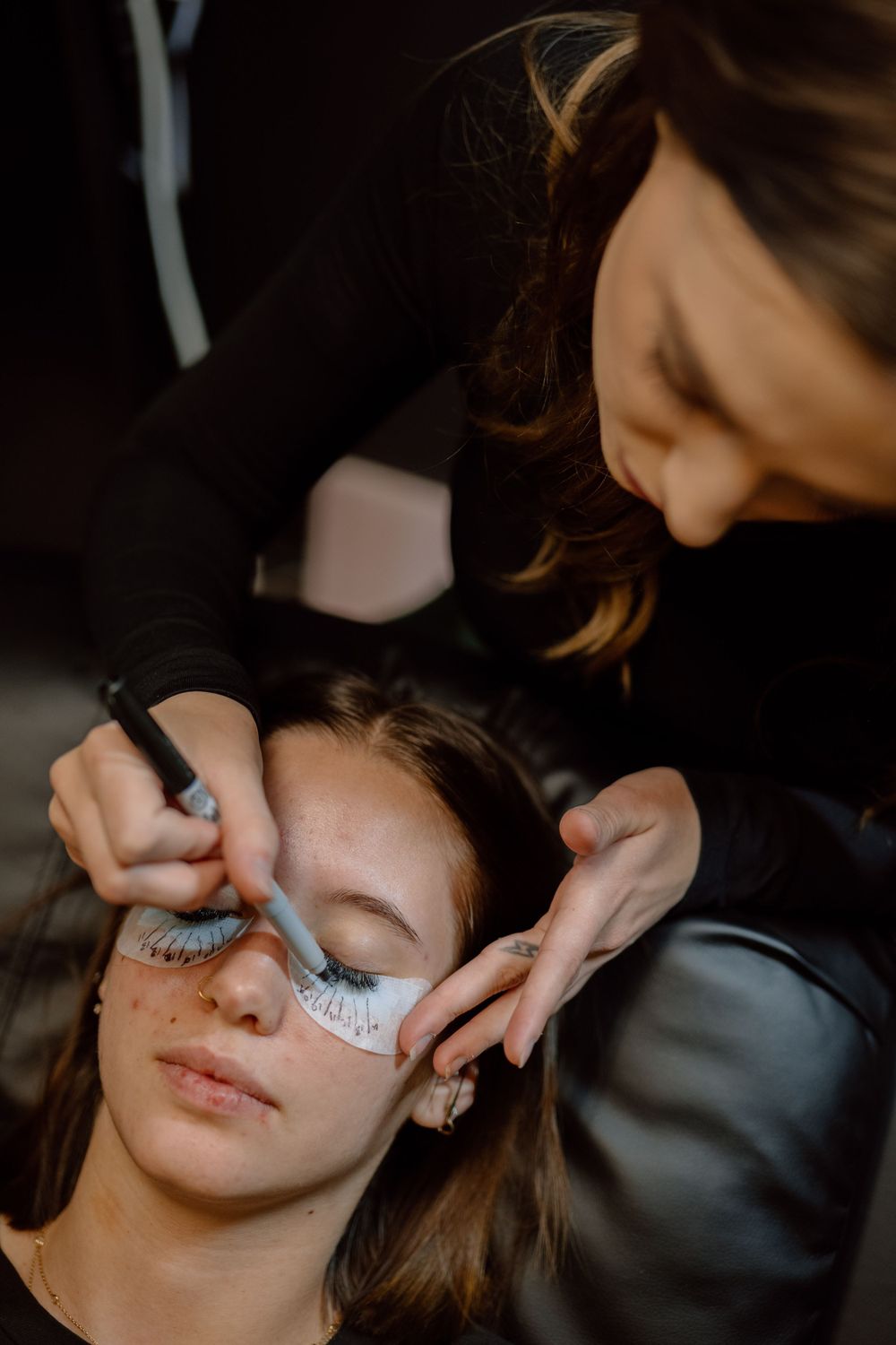 Makeup artist applying false eyelashes in warm ambient lighting.