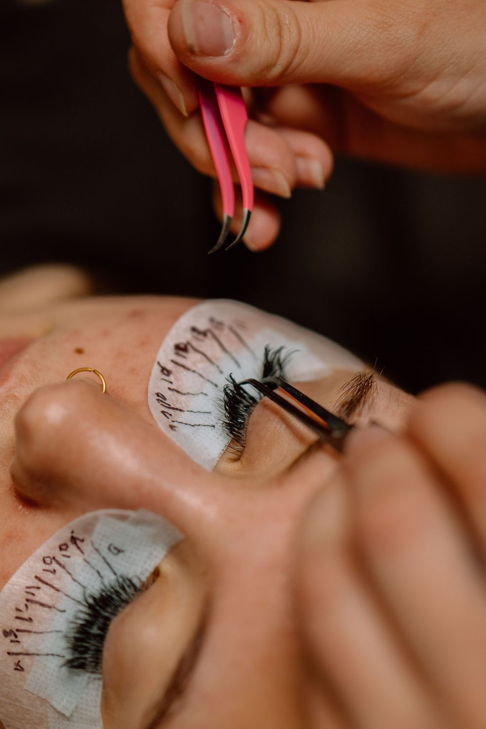Closeup of false eyelash application using pink tweezers and professional tools.