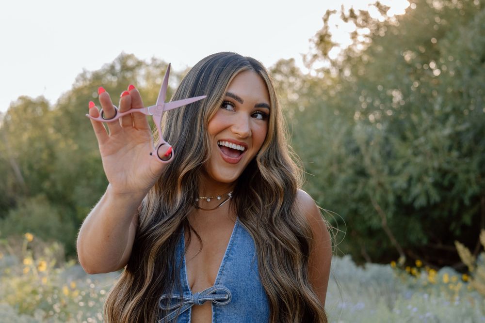 Person playfully holds scissors while smiling outdoors during golden hour.