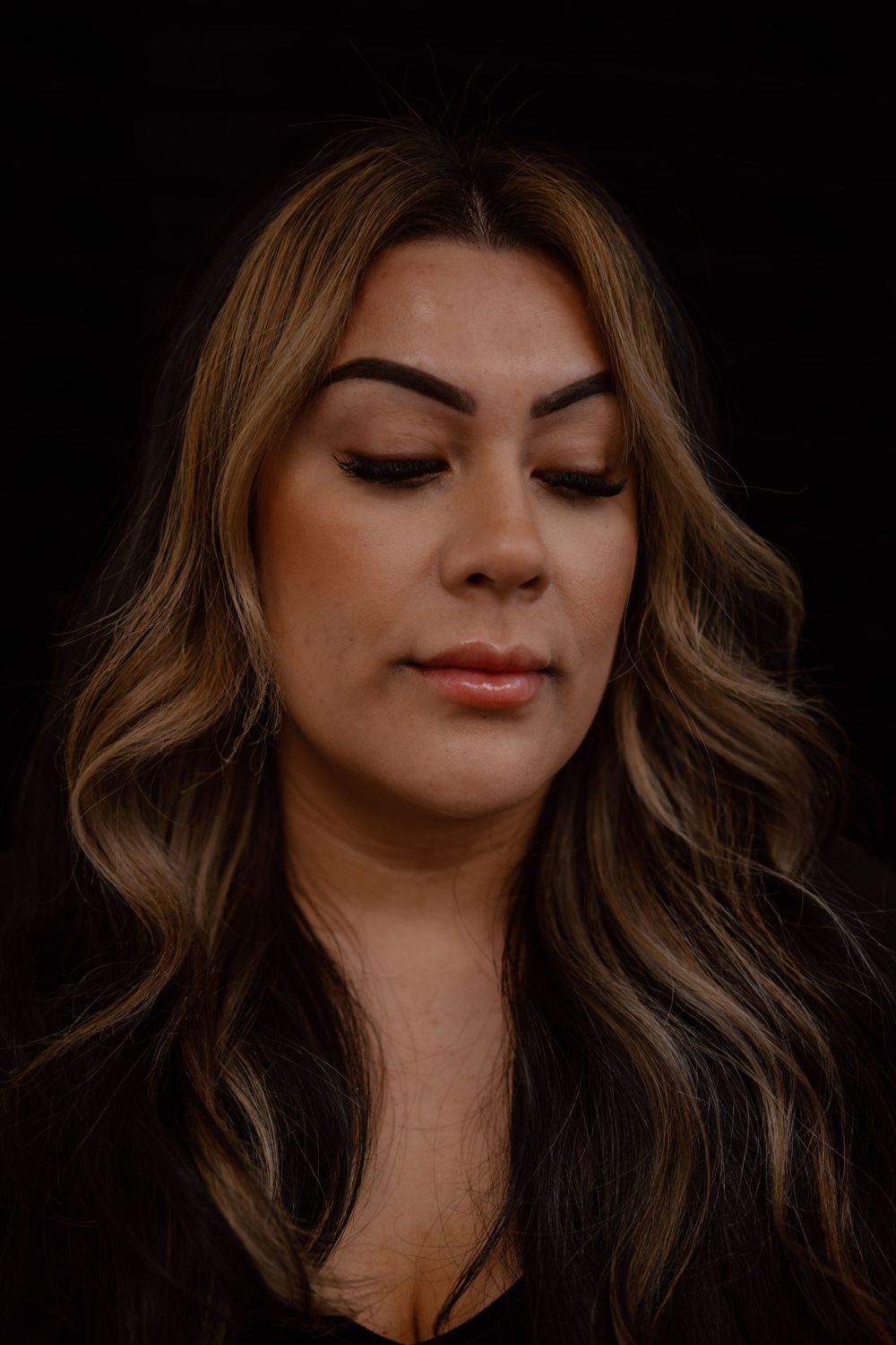 Artistic portrait showcasing professional makeup and wavy highlighted hair against dark background.