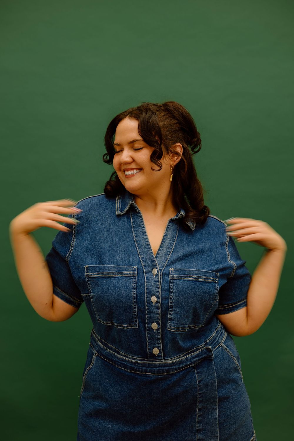 A joyful person wearing a denim jacket dances expressively against a green background.