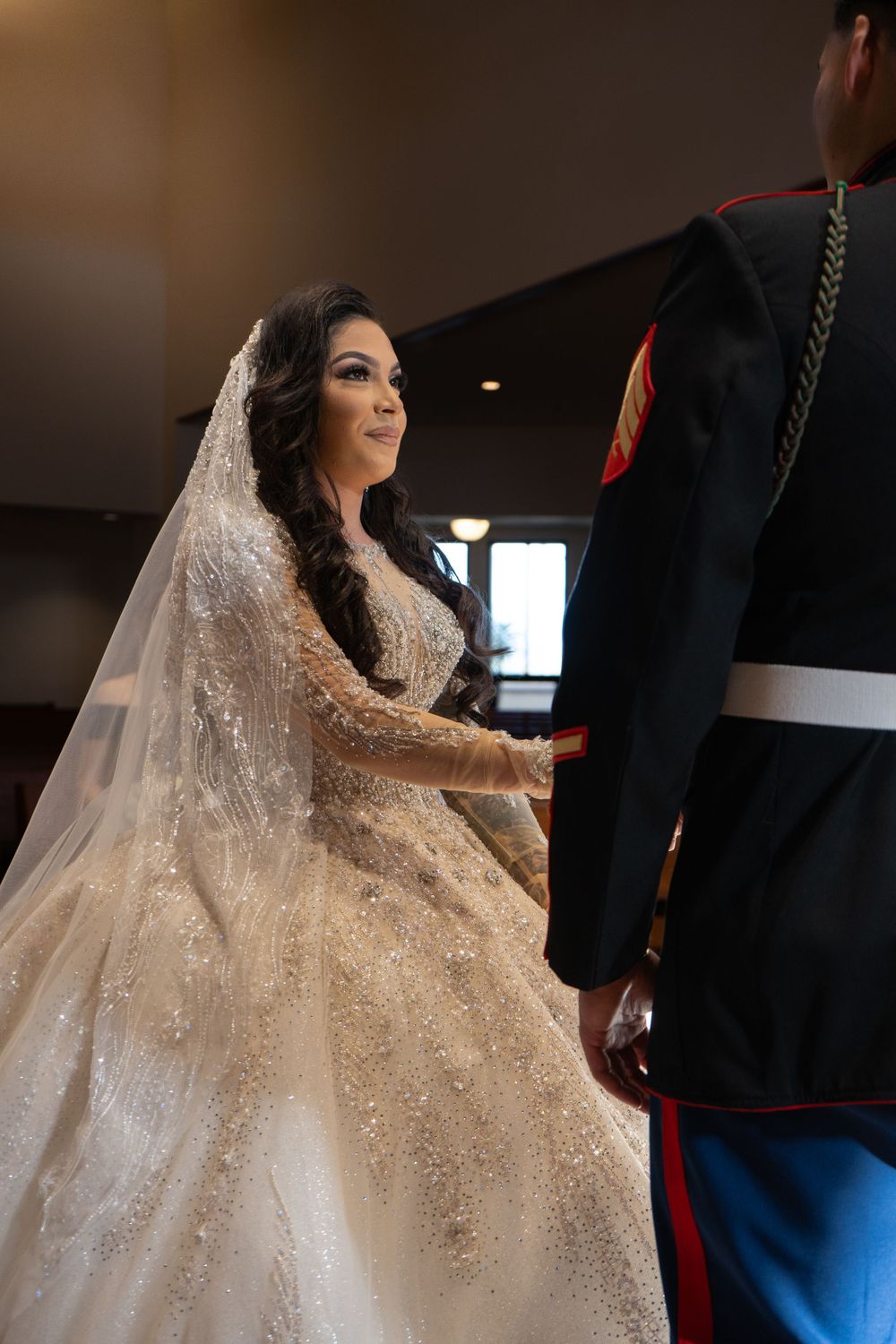 Bride in sparkly ballgown wedding dress poses dramatically in indoor setting.