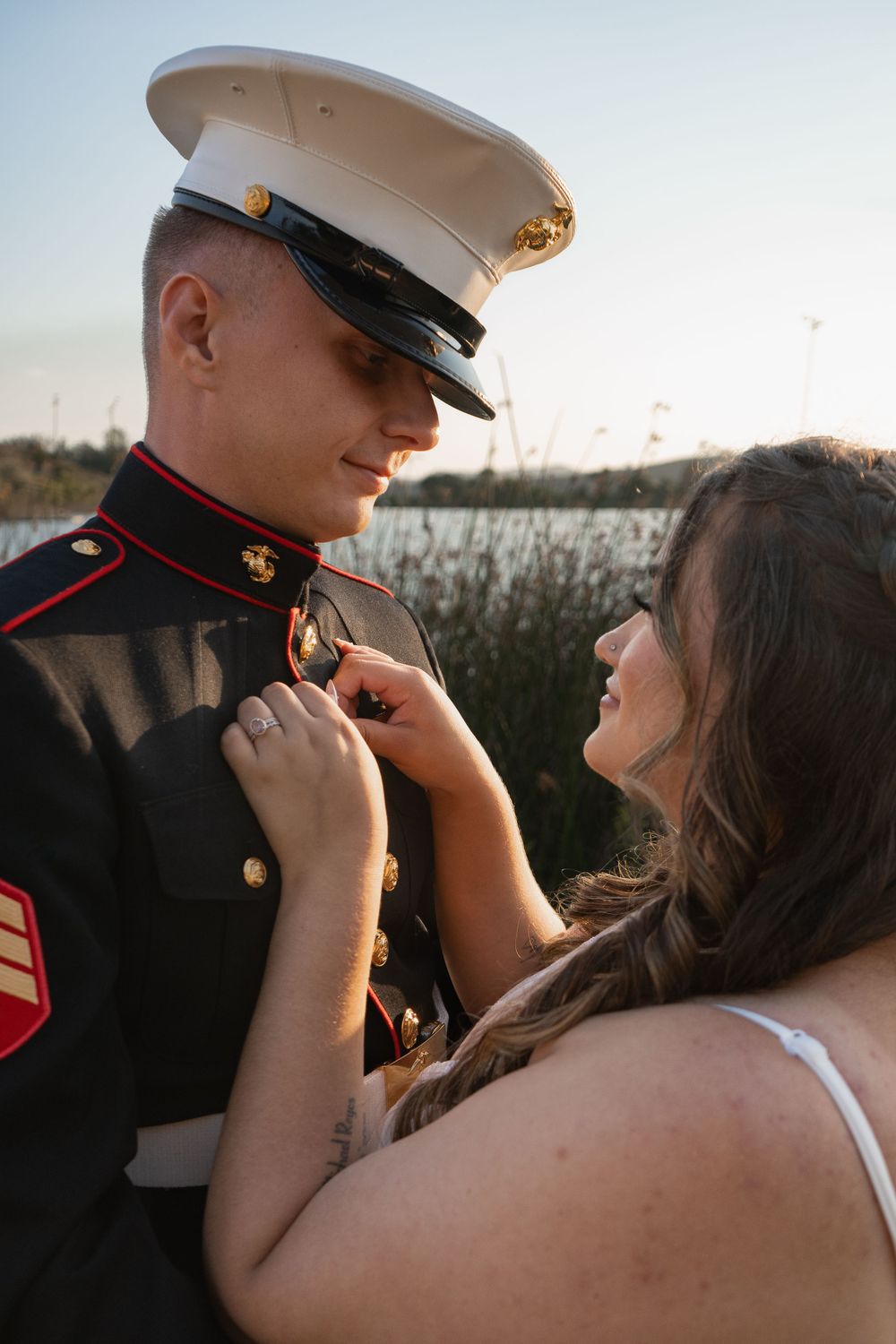 Marine in dress uniform shares a tender moment with someone outdoors during golden hour.